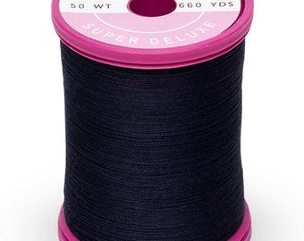 Puede incluir: Una bobina de hilo de algodón negro con una etiqueta rosa que dice "Cotton + Steel Super Deluxe 50 WT 660 YDS".