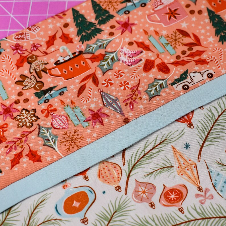May include: Two pieces of fabric with a Christmas theme. The top fabric is pink with a white background and features a variety of Christmas-themed illustrations, including candy canes, ornaments, and a gingerbread man. The bottom fabric is white with a green background and features a variety of Christmas ornaments.