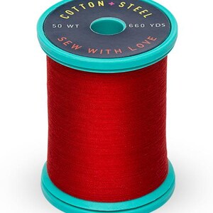 May include: A spool of red cotton thread with a teal base and top. The top of the spool has the text "Cotton + Steel", "50 WT", and "660 YDS". The text "Sew with Love" is also printed on the spool.