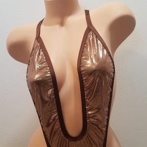 May include: A brown and gold metallic swimsuit with a plunging neckline and thin straps. The swimsuit has a shiny, iridescent finish.