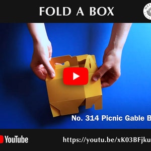 May include: A yellow cardboard box with a handle is being folded into a gable box shape. The box is labeled "No. 314 Picnic Gable Box". A YouTube play button is visible in the image. The text "https://youtu.be/xK03BFjkurM" is also visible.