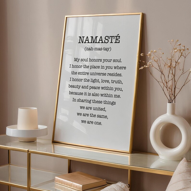 May include: A framed print with a gold frame and a white background. The print features the word "Namaste" in black text with the definition "(nah-mas-tay)" below it. The definition continues with the text: "My soul honors your soul. I honor the place in you where the entire universe resides. I honor the light, love, truth, beauty and peace within you, because it is also within me. In sharing these things we are united, we are the same, we are one."