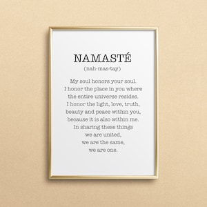 May include: A gold framed print with the word "Namaste" in black text, followed by the pronunciation in parentheses. The print includes a definition of the word, which is a Sanskrit greeting meaning "I bow to you".