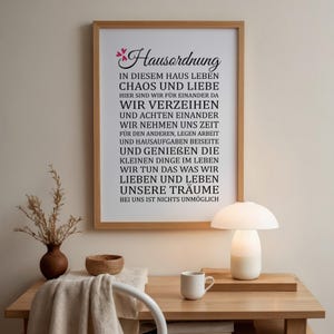 May include: A framed print with a white background and black text that reads "Hausordnung" in a decorative font. The text reads "In diesem Haus leben Chaos und Liebe. Hier sind wir f&uuml;r einander da. Wir verzeihen und achten einander. Wir nehmen uns Zeit f&uuml;r den anderen, legen Arbeit und Hausaufgaben beiseite. Und genie&szlig;en die kleinen Dinge im Leben. Wir tun das was wir lieben und leben unsere Tr&auml;ume. Bei uns ist nichts unm&ouml;glich."