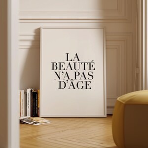 Puede incluir: Una impresi&oacute;n enmarcada en blanco con texto negro que dice "LA BEAUT&Eacute; N'A PAS D'&Acirc;GE". La impresi&oacute;n est&aacute; colgada en una pared blanca con moldura blanca.