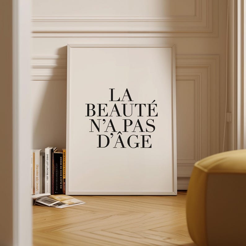 Puede incluir: Una impresi&oacute;n enmarcada en blanco con texto negro que dice "LA BEAUT&Eacute; N'A PAS D'&Acirc;GE". La impresi&oacute;n est&aacute; colgada en una pared blanca con moldura blanca.