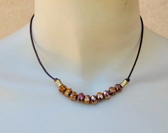 May include: A brown leather cord necklace with a row of iridescent brown glass beads and gold metal accents.
