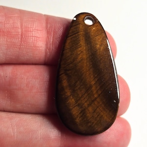 May include: A teardrop-shaped pendant made of brown tiger's eye gemstone with a hole at the top for stringing.