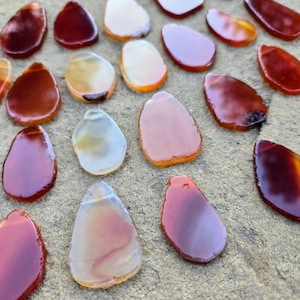May include: A collection of carnelian gemstone chips in various shades of red, orange, and white. The chips are irregularly shaped and have a smooth, polished finish.