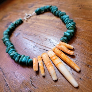 May include: A turquoise and orange shell necklace with a silver clasp. The necklace is made of turquoise stones and orange shell pieces. The shell pieces are arranged in a fan shape.