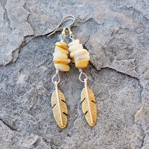 May include: Gold and white feather earrings with a stacked stone design. The stones are a mix of white and gold.