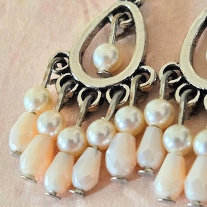 May include: Silver dangle earrings with a teardrop-shaped design and multiple rows of white pearl beads.