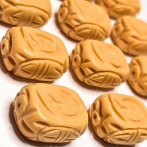 May include: A collection of ten carved, light brown, rectangular beads. The beads have a textured, intricate design.