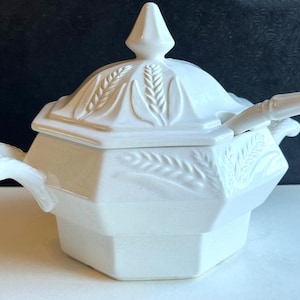 May include: A white ceramic sugar bowl with a matching lid and a small spoon. The bowl features an octagonal shape with embossed wheat stalk patterns on the lid and sides. It includes two side handles and a pointed finial on the lid top.