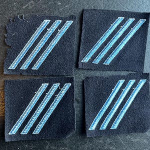 May include: Four dark blue fabric patches with three light blue stripes sewn on each. The stripes are angled diagonally across the patches.