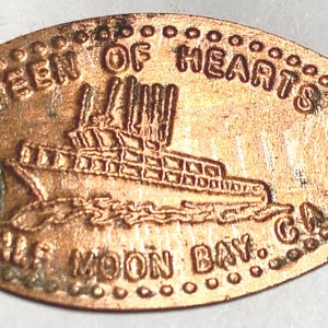 May include: A copper elongated penny with the text "QUEEN OF HEARTS HALF MOON BAY, CA." A boat is depicted in the center. The penny has a dotted border and is slightly tarnished.