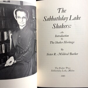 K&ouml;nnte beinhalten: Schwarz-Wei&szlig;-Foto eines ge&ouml;ffneten Buches mit dem Titel "The Sabbathday Lake Shakers: An Introduction to The Shaker Heritage" von Sister R. Mildred Barker. Eine Frau in dunklem Kleid und Haube ist links zu sehen.