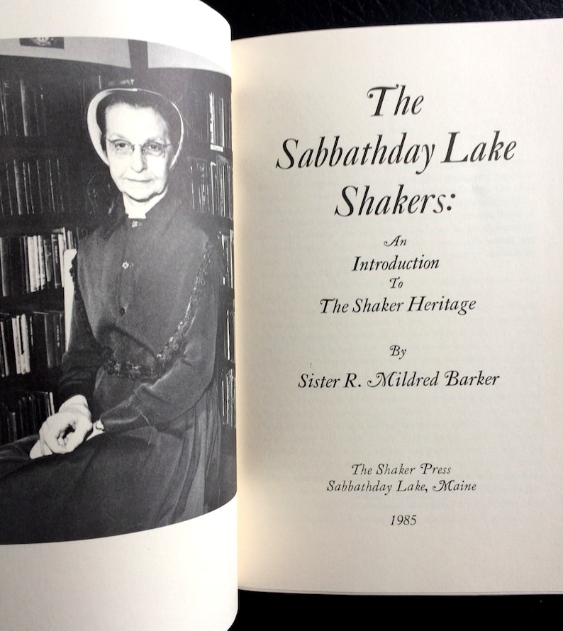 K&ouml;nnte beinhalten: Schwarz-Wei&szlig;-Foto eines ge&ouml;ffneten Buches mit dem Titel "The Sabbathday Lake Shakers: An Introduction to The Shaker Heritage" von Sister R. Mildred Barker. Eine Frau in dunklem Kleid und Haube ist links zu sehen.