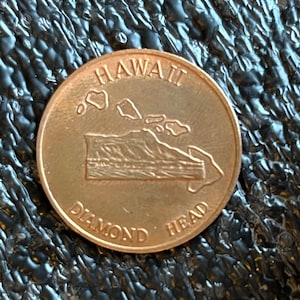 May include: A copper-colored coin with the words "HAWAII" and "DIAMOND HEAD" around the edge. The coin features a raised image of the island of Oahu, Hawaii, with Diamond Head in the foreground.