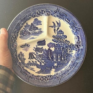 May include: Blue and white divided plate with a Willow pattern design. The plate features three sections and a detailed landscape scene with pagodas, bridges, and birds. The rim has a decorative border.