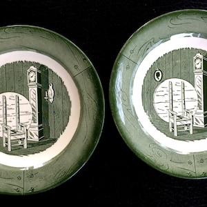 May include: Two green and white decorative plates. Each plate features a central design of a room with a grandfather clock, chair, and table. The outer rim has a wood grain pattern.
