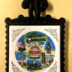 May include: Black metal trivet with a white tile featuring a colorful illustration of Boston landmarks, including the U.S. Constitution, Bunker Hill Monument, and the State House. The tile also displays the words "Boston Mass Beans".
