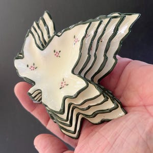 May include: A stack of six white ceramic leaf-shaped dishes with a green rim and pink floral pattern.