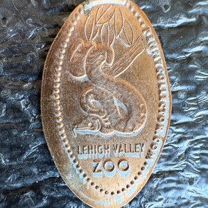 May include: Elongated copper penny from the Lehigh Valley Zoo. The penny features a detailed embossed design of a snake coiled around a tree branch. The text "LEHIGH VALLEY ZOO" is also embossed on the penny.