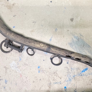 May include: A wooden ox yoke with metal rings and a rounded end. The yoke is weathered and shows signs of use.