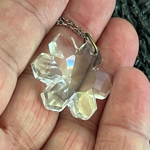 May include: A clear crystal snowflake pendant on a silver chain. The snowflake is faceted and has a delicate, intricate design.