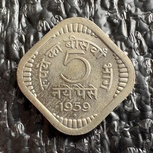 May include: A silver-colored, diamond-shaped coin with the number 5 prominently displayed in the center. The coin features Hindi script around the edges and the year 1959 at the bottom. The coin is slightly worn.