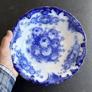 May include: Antique blue and white porcelain plate with a floral design. The plate features a scalloped edge and a central bouquet of flowers. The blue and white color scheme gives the plate a classic, vintage look.