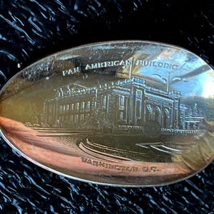 May include: Silver spoon with an engraved image of the Pan American Building in Washington, D.C. The spoon's bowl features the building's facade, with the text "PAN AMERICAN BUILDING" and "WASHINGTON D.C." engraved above and below the building.