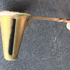 May include: A vintage brass tool with a cone-shaped body and a handle. The tool has a slot cut down the side of the cone. The handle is twisted. The tool is held by a person's hand.