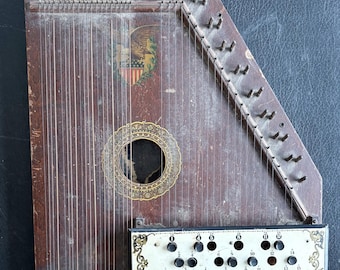 May include: Antique wooden autoharp with a dark brown finish. The instrument features numerous strings, tuning pegs, and a decorative sound hole. A metal plate with numbered buttons is visible. The autoharp has an eagle emblem and the text "PATENTED-PATENTS PENDING".