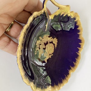 May include: A cobalt blue porcelain dish with a gold rim and a gold floral design. The dish has a handle and is shaped like a leaf.