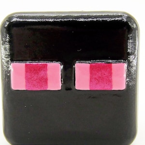 May include: Black square-shaped charm with two pink eyes. The charm is made of polymer clay and has a glossy finish.