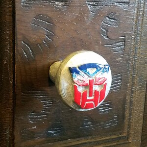 May include: A round, silver drawer knob with a red, blue, and silver robot face design.
