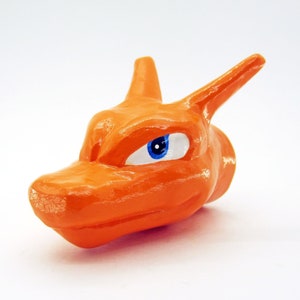 May include: Orange ceramic figurine of a cartoon character with a blue eye. The character has a pointed snout and ears.
