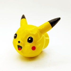 May include: A yellow Pikachu figurine with black ears and eyes, and red cheeks. The figurine is made of a smooth, painted material.
