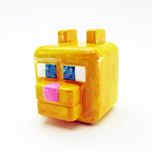 May include: A yellow Minecraft-style figure of a cat with blue eyes and a pink nose.