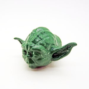 May include: A green Yoda figurine with large ears. The figurine is made of plastic and has a detailed face.