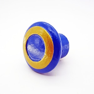 May include: A blue and gold wooden knob with a circular design. The knob is a decorative accent for furniture or cabinets.