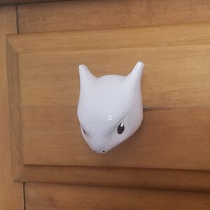 May include: A white ceramic drawer pull shaped like a cartoon creature with black eyes and a pink nose.
