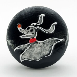 May include: A black round wooden knob with a white and gray image of Zero, the ghost dog from Nightmare Before Christmas, with a red collar. Zero is holding a glowing orange orb in his mouth.