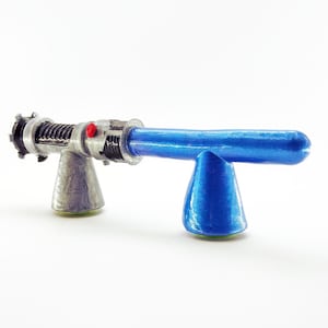 May include: A blue and silver toy lightsaber with a red button on the handle. The lightsaber is on a blue stand.