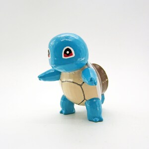 Op de afbeelding: Een klein, blauw en bruin beeldje van een schildpad met rode ogen. De schildpad staat op zijn achterpoten en heeft zijn voorpoten uitgestrekt.