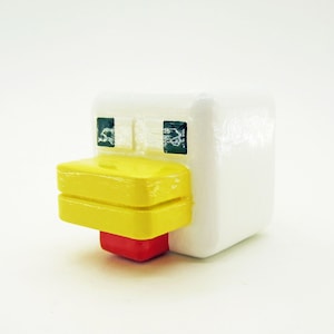 May include: A white chicken figurine with a yellow beak and red wattle. The chicken has black eyes and a simple design.