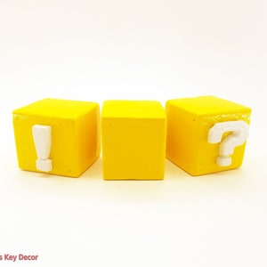 May include: Three yellow block-shaped toys with white question mark and exclamation point symbols. The blocks are made of plastic and are about 2 inches tall.