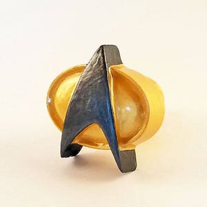 May include: A gold ring featuring a black Starfleet insignia. The ring is a popular piece of Star Trek jewellery.